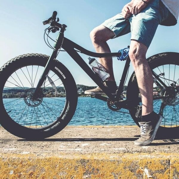 Person sitting on a black bicycle by a body of water with a clear blue sky.