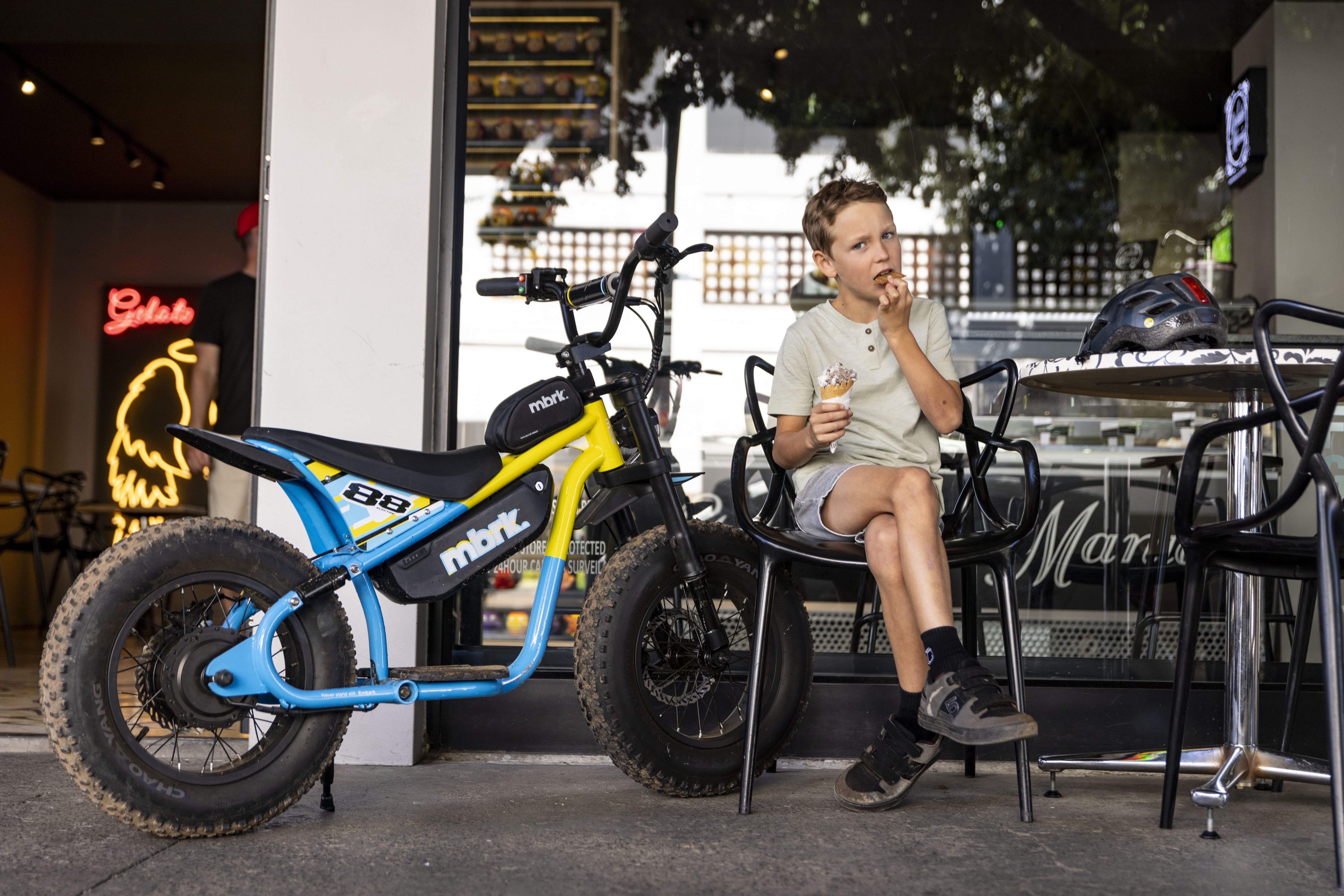 Person sitting on a chair next to a small motorcycle in an outdoor cafe setting