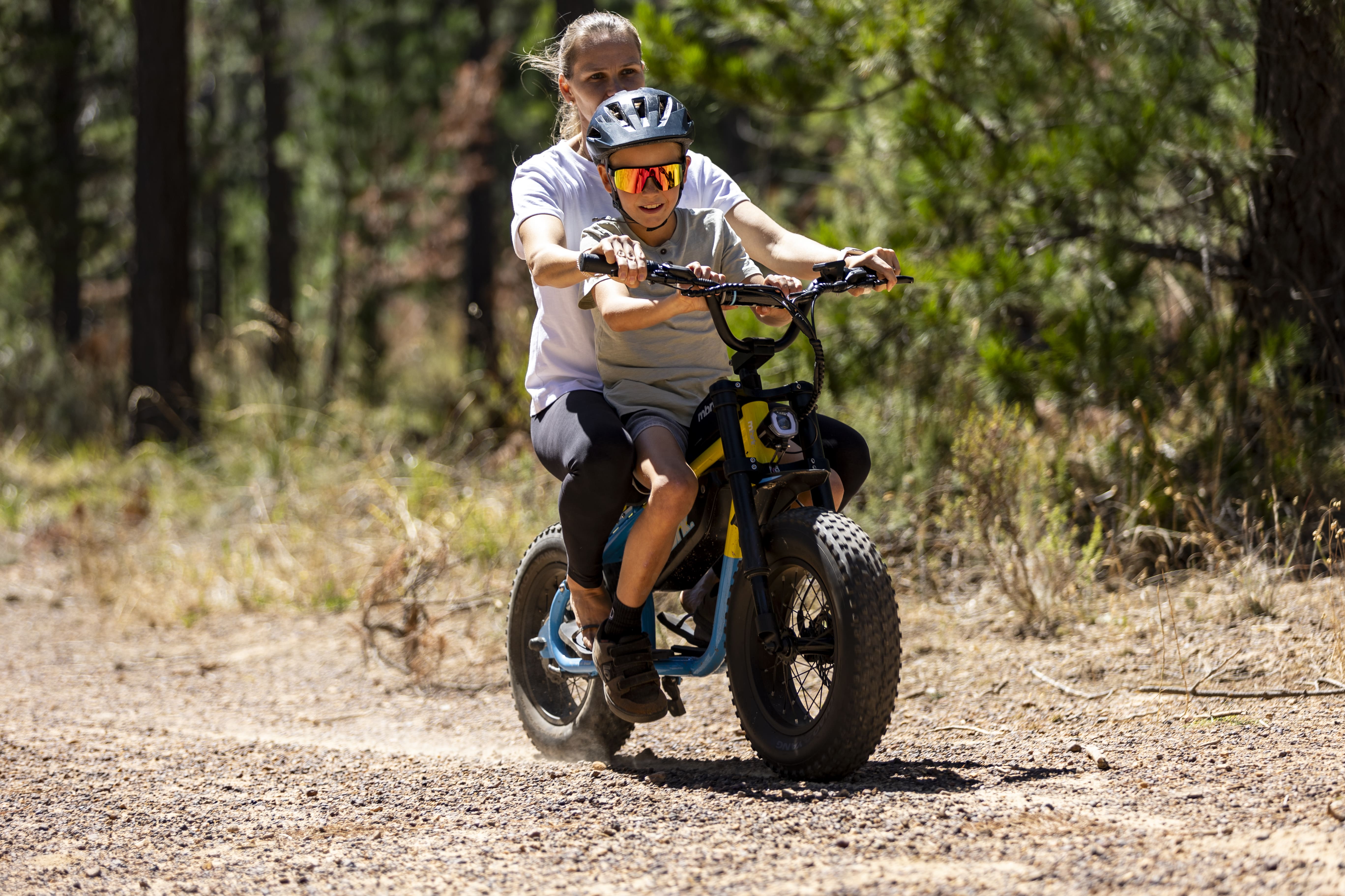 Child riding a balance bike on a dirt path with trees in the background