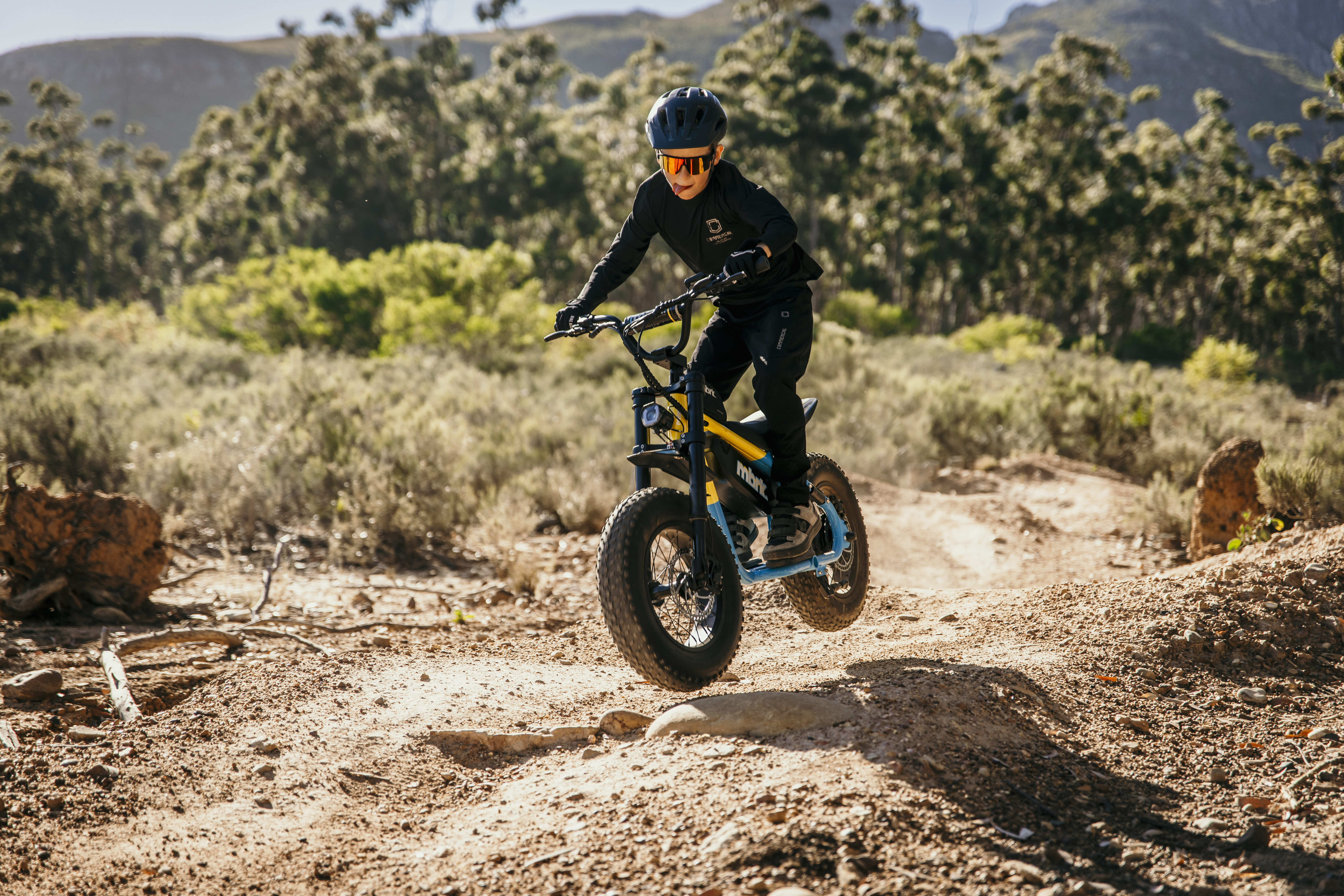 Person riding a mini bike on a dirt trail with trees and mountains in the background